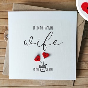 May include: A white card with black text that reads "To the most amazing wife on your 30th birthday". Two red heart-shaped buttons are attached to the card, representing flowers in a pot.
