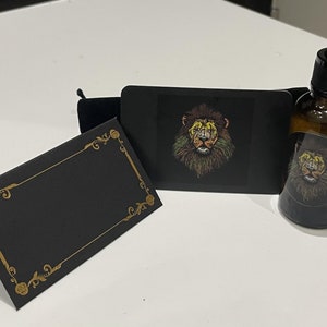 May include: A black card with a gold border and a lion graphic. The lion has green, yellow, and orange fur. The card is next to a small brown glass bottle with a black dropper and a lion graphic label. The bottle is sitting on a white surface.