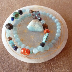 Peut inclure: Deux bracelets avec des perles bleues et vertes, une pierre bleu clair et une pierre brune et orange sur une pierre ronde blanche avec un motif doré.