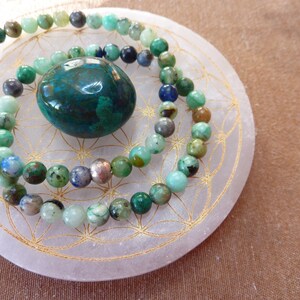 Puede incluir: Dos pulseras de piedras preciosas verdes con una piedra preciosa verde más grande en el centro, todas descansando sobre una piedra circular blanca con un patrón geométrico dorado.