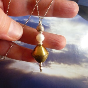 May include: A silver chain necklace with a gold pendant. The pendant is a teardrop shape with a pearl and two silver beads.