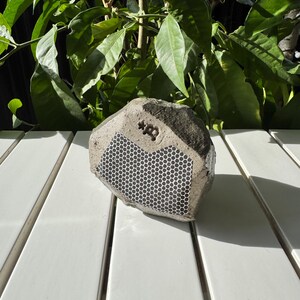 May include: A gray concrete speaker shaped like a rock with a black honeycomb pattern and the text "*B" on the front.