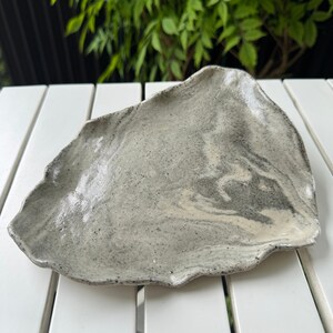 Peut inclure: Un plat de service en céramique gris et blanc avec une forme irrégulière et organique. Le plat a un glaçage moucheté et marbré.