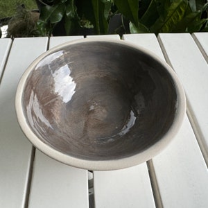 May include: A large, round, grey ceramic bowl with a white rim. The bowl has a smooth, glossy finish and is slightly textured.