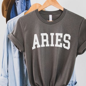 K&ouml;nnte beinhalten: Ein graues T-Shirt mit dem Wort "ARIES" in wei&szlig; auf der Vorderseite.