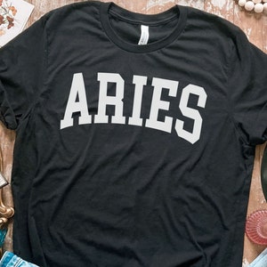 K&ouml;nnte beinhalten: Schwarzes T-Shirt mit wei&szlig;em Text, der "ARIES" in einer College-Schriftart lautet.