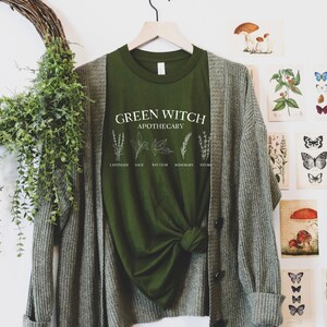 May include: Green t-shirt with the text "Green Witch Apothecary" and illustrations of herbs, including lavender, sage, bay leaf, rosemary, and thyme.