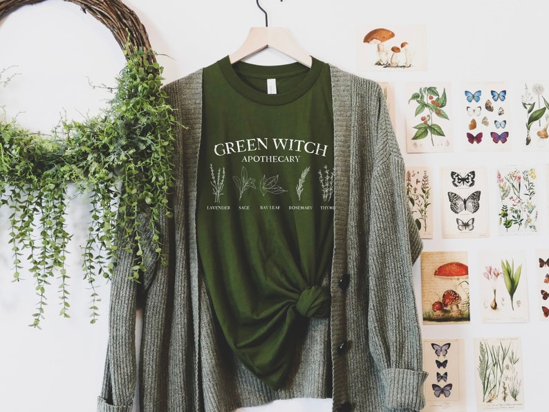 May include: Green t-shirt with the text "Green Witch Apothecary" and illustrations of herbs, including lavender, sage, bay leaf, rosemary, and thyme.