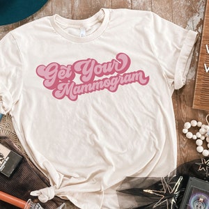 May include: A white t-shirt with a pink retro-style graphic that says "Get Your Mammogram".