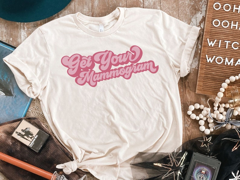 May include: A white t-shirt with a pink retro-style graphic that says "Get Your Mammogram".