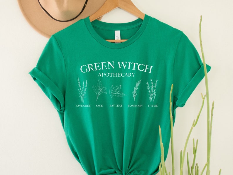 May include: Green t-shirt with the text "Green Witch Apothecary" and illustrations of herbs labeled "Lavender", "Sage", "Bay Leaf", "Rosemary", and "Thyme".