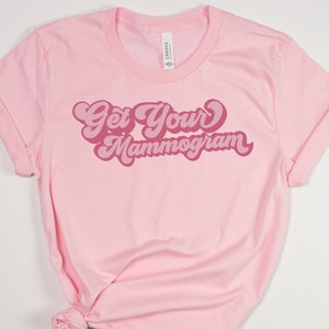 May include: Pink t-shirt with the text "Get Your Mammogram" in a retro pink font.
