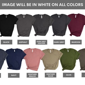 K&ouml;nnte beinhalten: Ein Mockup von zehn T-Shirts in verschiedenen Farben, darunter Schwarz, Asphalt, Dunkelgrau meliert, Dunkelgrau, Rotbraun, Dunkelblau meliert, Dunkelblau, Flieder meliert, Oliv meliert, Oliv und Armeegr&uuml;n. Der Text "IMAGE WILL BE IN WHITE ON ALL COLORS" wird &uuml;ber den T-Shirts angezeigt.