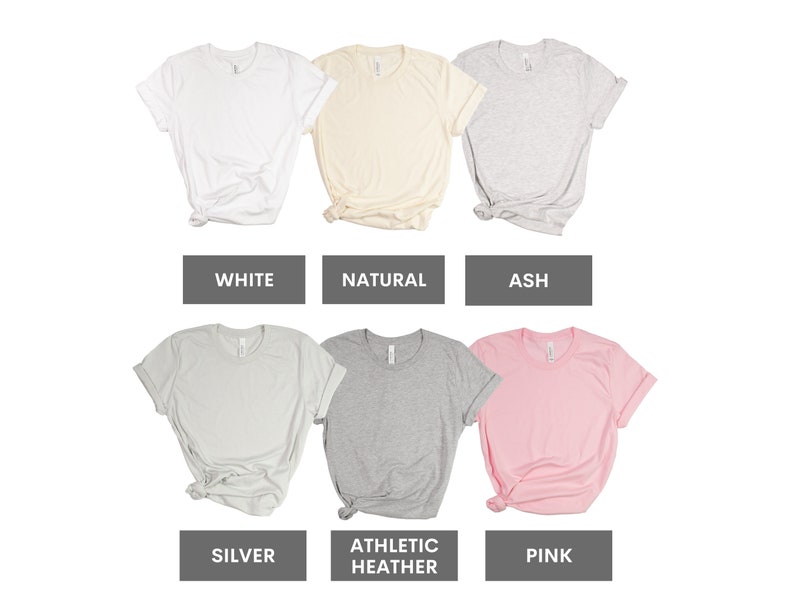 May include: Six different color t-shirts, including white, natural, ash, silver, athletic heather, and pink. The shirts are all folded and laid out on a white background.