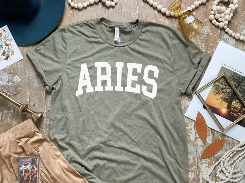 K&ouml;nnte beinhalten: Ein gr&uuml;nes T-Shirt mit dem Wort "ARIES" in wei&szlig; auf der Vorderseite.