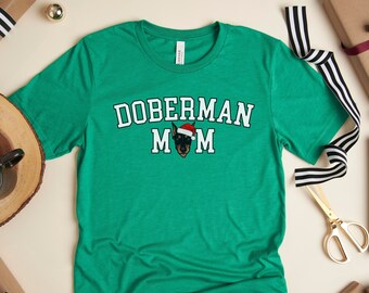 May include: Green t-shirt with the text "Doberman Mom" in white letters with a Doberman wearing a Santa hat in the middle of the text.