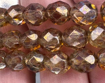 May include: Close-up of strands of faceted, amber-colored beads. The beads have a multi-faceted design, catching light and creating a shimmering effect. The beads are strung together, suggesting they are for jewelry making or crafting.