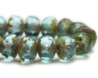 May include: A strand of faceted, oval-shaped beads. The beads have a light blue hue with a mottled, iridescent finish. The beads are strung together, and the image is set against a white background.
