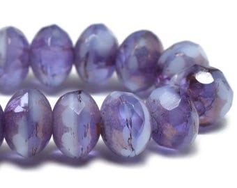 May include: Close-up of a strand of faceted beads in shades of purple and white. The beads have an oval shape with multiple facets, creating a sparkling effect. The beads are strung together, suggesting they are for jewelry making.