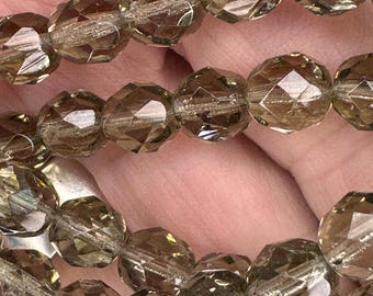 May include: Close-up of several strands of faceted, smoky quartz beads. The beads are a translucent, warm brown color and have a multi-faceted cut that catches the light. The beads are strung together, creating a necklace or bracelet.