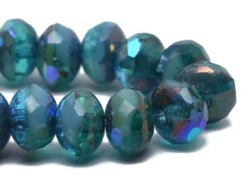 May include: Close-up of a strand of faceted beads in shades of teal and blue. The beads have an iridescent finish, reflecting multiple colors. The beads are oval-shaped and have a polished, shiny appearance. Ideal for jewelry making.