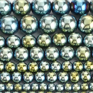 May include: A close-up of a collection of round, iridescent beads in shades of blue and green. The beads have a metallic sheen and are arranged in rows.