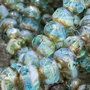 May include: A strand of iridescent glass beads with a light blue and gold color scheme. The beads have a faceted design and are strung on a clear thread.