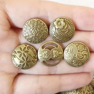 May include: Five antique gold-toned metal buttons with intricate floral designs. The buttons have a raised, textured surface and are perfect for adding a vintage touch to clothing or crafts.