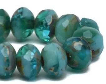 May include: Close-up of a strand of faceted beads in shades of teal, turquoise, and brown. The beads have an oval shape and a glossy finish, reflecting light. These beads are suitable for jewelry making.