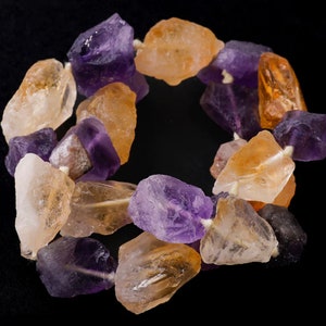 May include: A strand of natural gemstone beads, featuring a mix of amethyst, citrine, and clear quartz. The beads are irregular in shape and have a rough, natural finish.