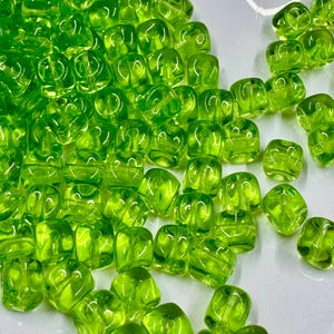 May include: A large group of lime green glass beads in a square shape. The beads are translucent and have a slight shimmer to them.