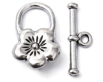 May include: A silver-toned toggle clasp set. The clasp features a flower-shaped design with a central sunburst pattern. The bar component has a rounded end and a small loop. Ideal for jewelry making.