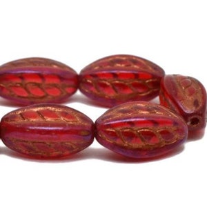 May include: A strand of red glass beads with a gold leaf design. The beads are oval shaped and have a glossy finish.