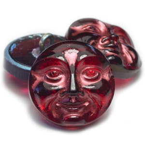 May include: Three red glass buttons with a face design. The buttons are round and have a raised face with eyes, nose, and mouth.
