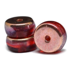May include: Two red glass beads with a copper metallic finish. The beads are round with a hole in the center.