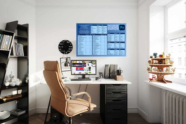 Op de afbeelding: Een thuiskantoorwerkplek met een wit bureau, een zwarte bureaustoel, een computermonitor, een zwarte lamp en een boekenkast met boeken. Een poster met de tekst "Photoshop-toetsenbordshortcuts" hangt aan de muur.