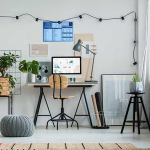 Op de afbeelding: Een thuiskantoor met een computer, bureau, stoel en planten. Een poster met de tekst "Ps" hangt aan de muur.