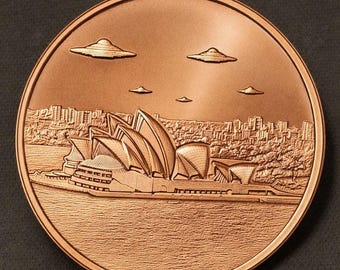 May include: A circular copper-toned commemorative coin featuring a relief of the Sydney Opera House on the waterfront. Above the building, five unidentified flying objects shaped like flying saucers are depicted in the sky over the city skyline.