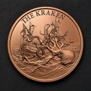 May include: A round copper-toned coin featuring a relief design of a giant kraken attacking a sailing ship. The text THE KRAKEN is embossed along the top edge. The scene depicts tentacles wrapping around the masts and hull of the vessel.