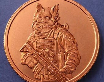 May include: A circular copper-toned coin featuring a detailed relief of a cat dressed in tactical military gear. The cat is depicted wearing a vest with pouches and holding a rifle. A small paw print emblem is visible on the shoulder patch.