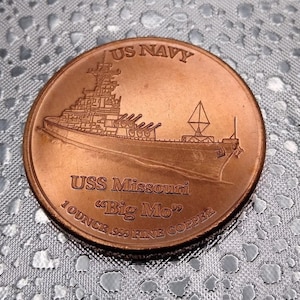 Puede incluir: Una moneda de color cobre con una representaci&oacute;n del acorazado USS Missouri y el texto "US NAVY" y "USS Missouri "Big Mo" 1 OUNCE .999 FINE COPPER".