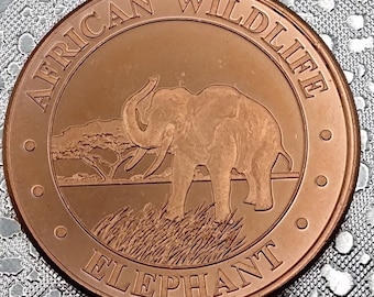 May include: A copper-colored coin with the words "African Wildlife Elephant" around the edge. The center of the coin features an image of an elephant standing in tall grass with trees in the background.