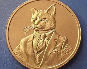 May include: A circular bronze-toned coin featuring a relief engraving of a cat with pointed ears wearing a formal suit, a collared shirt, and a striped necktie. The cat is depicted from the chest up, showcasing detailed fur texture and whiskers.