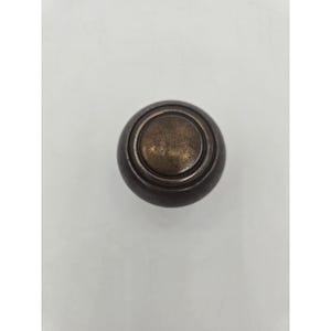 May include: A round, antique-style cabinet knob with a dark bronze finish. The knob features a circular design with concentric rings and a slightly raised center, suitable for furniture restoration or new builds.