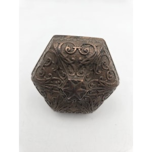 May include: A bronze-colored, multi-sided box with ornate, swirling patterns and a star design on the top. The box has a metallic finish and is set against a white background.