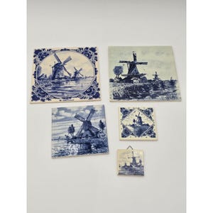 May include: Five square and rectangular ceramic tiles featuring blue and white illustrations of Dutch windmills in various landscapes. The tiles display detailed scenes of water, trees, and structures, with some featuring decorative floral borders.