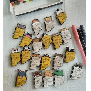 May include: A collection of 16 small wooden notebooks with colorful animal illustrations and positive messages. Each notebook has a spiral binding and a yellow background. The messages include "You are awesome", "You rock", "Make a new friend today", "Be a good listener", "Be a good friend", "Be a shining star today", "I love you", "Have a happy day", "A big hug for you", "You've got this", "Give it your all", "Share a smile today", "Good luck today", "Do your best", "Keep up the good work", "I am proud of you", "Have a super day", and "You are amazing".