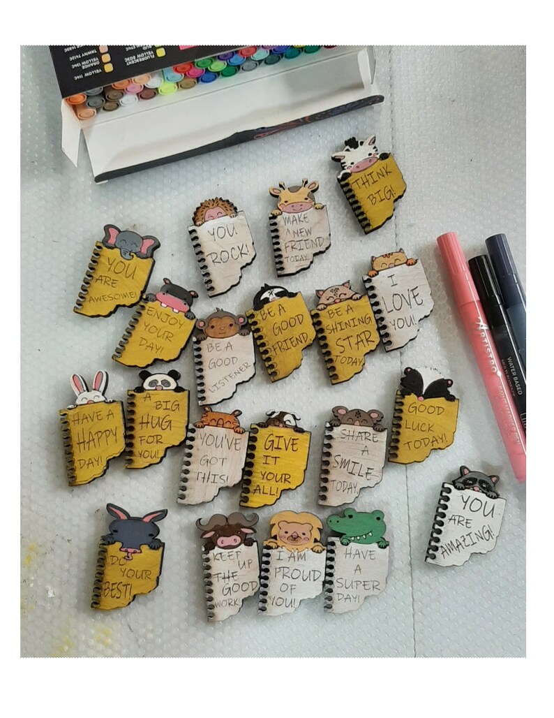 May include: A collection of 16 small wooden notebooks with colorful animal illustrations and positive messages. Each notebook has a spiral binding and a yellow background. The messages include "You are awesome", "You rock", "Make a new friend today", "Be a good listener", "Be a good friend", "Be a shining star today", "I love you", "Have a happy day", "A big hug for you", "You've got this", "Give it your all", "Share a smile today", "Good luck today", "Do your best", "Keep up the good work", "I am proud of you", "Have a super day", and "You are amazing".