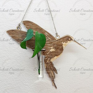Puede incluir: Un recorte de madera de colibrí con un tubo de vidrio para jarrón. El colibrí está colgado de una cuerda y tiene una planta verde en el jarrón. La imagen incluye el texto "SVG PNG PDF EPS DXF" y "Schott Creations Digital" repetido varias veces. El texto "Descarga digital" también está incluido.