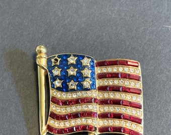Broche de bandera ondeante en tono rojo, blanco, azul y dorado.